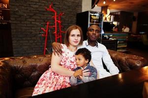 Lycklig multietnisk familj med pojke unge spendera tid på restaurang. relationer av afrikansk man och vit europeisk kvinna. foto