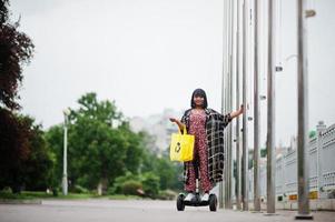 vacker afrikansk amerikansk kvinna som använder segway eller hoverboard. svart flicka med gul duk eco väskor återvinning symbol. foto