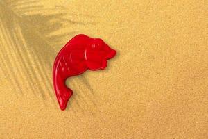 röd plast fisk på sand strand bakgrund, närbild. barns leksaker för badning bebisar. pedagogisk spel för barn, förskola utbildning. layout, förberedelse av leksaker för de designer eller hemsida foto