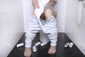 kvinna pissande, med diarre på en vit toalett skål i de toalett med en rulla av papper i henne hand. foto