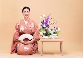 ung 20s asiatisk japansk kvinna ha på sig traditionell kimono, gör ikebana blomma arrangemang foto