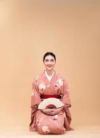 ung 20s asiatisk japansk kvinna ha på sig traditionell kimono, gör sitta på golv foto