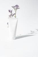 fuktkräm hand grädde vit plast rör attrapp på vit trandy bakgrund med blomma och hård skuggor. tom hud vård skönhet produkt förpackning foto