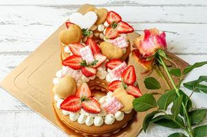 svamp kaka med jordgubbar, rosa choklad barer, vanilj grädde och hjärta chape småkakor i form av siffra 8 med rosa reste sig. en gåva för särskild ett för internationell kvinnor dag. ljuv närvarande foto