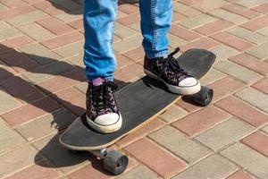 flicka i svart gymnastikskor på en skateboard. fötter på en skateboard. foto