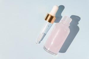 topp se av transparent dropper flaska med rosa skönhet ansikte olja på blå bakgrund. anti åldring serum med naturlig ingredienser. foto