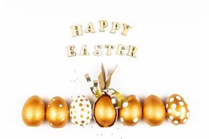 påsk festlig dekoration. topp se av påsk ägg färgad med gyllene måla och inskrift i engelsk Lycklig påsk. trä- brev på vit bakgrund. olika prickad design foto