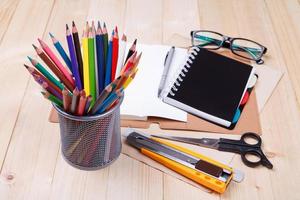 arbetsplats med färgad pennor och förnödenheter, anteckningsbok, monokel på trä- tabell foto