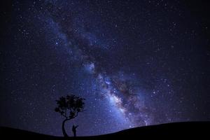 en man är stående unter träd pekande på en ljus stjärna med mjölkig sätt galax och Plats damm i de universum foto