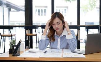 ung asiatisk affärskvinna som arbetar på en surfplatta, är stressad har huvudvärk och tänker hårt på kontoret. foto