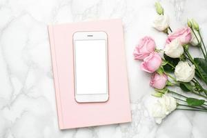mobil telefon med rosa och vit ro blommor på marmor bakgrund.minimalistisk sammansättning för de helgdagar, alla hjärtans dag dag och kvinnor dag. foto