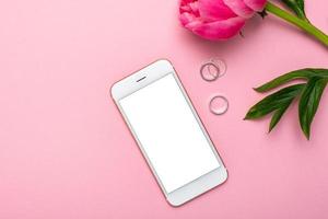 mobil telefon falsk upp och pion blomma på rosa pastell tabell i platt lägga stil. kvinna arbetssätt skrivbord.sommar Färg foto