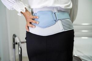 asiatisk dampatient som bär ryggvärkstödbälte för ortopedisk ländrygg med rullator. foto