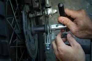 närbild tekniker arbetare hand, fast motocykel hjul på utsidan av garaget. foto