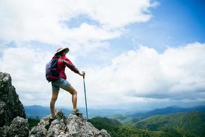 ung person vandring kvinna stående på toppen rock, ryggsäck kvinna tittar på vackra bergsdalen i solljus på sommaren, landskap med sport flicka, höga kullar, skog, himmel. resor och turism. foto