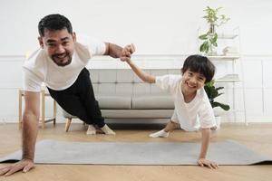 ung asiatisk thai far härlig tåg henne liten son till övning och praxis yoga på levande rum golv tillsammans för friska kondition och friskvård, Lycklig inhemsk Hem livsstil på familj helger. foto