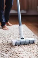 mänsklig ben och en vit turbo borsta av en sladdlös Vakuum rengöringsmedel rengör de matta i de hus foto