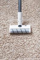 en sladdlös Vakuum rengöringsmedel rengör de matta i de levande rum med de botten av de ben. foto