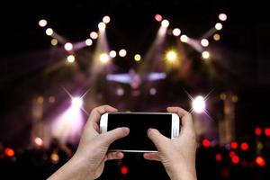 händer som håller mobil smartphone med ljus bokeh i konsertoskärpa bakgrund foto