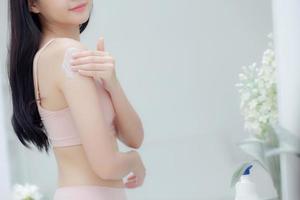 vacker sexig ung asiatisk kvinna spegelvänd applicera kräm på axeln och meddelande, skönhetsflicka applicerar kroppslotion hudvård för hälsa och mjuk återfuktning, behandling och kosmetika med fuktkräm. foto