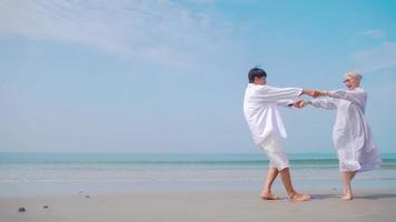 asiatisk pensionerad par avkopplande förbi de hav i sommar. en senior kvinna dans med henne partner på de strand. foto