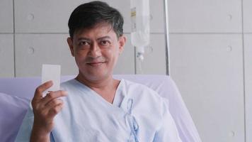 äldre asiatisk manlig patient innehav liv försäkring kort under sjukhusvistelse. foto