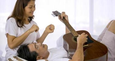 Lycklig asiatisk älskare spelar gitarr och sång låtar tillsammans i en sovrum. foto