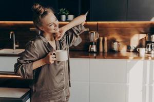 ung ganska avslappnad kvinna i pyjamas med en kopp kaffe på morgonen foto