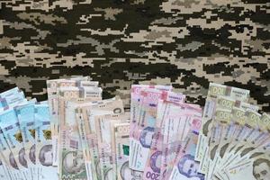 ukrainska hryvnya räkningar på tyg med textur av ukrainska militär pixeled kamouflage. trasa med camo mönster i grå, brun och grön pixel former foto