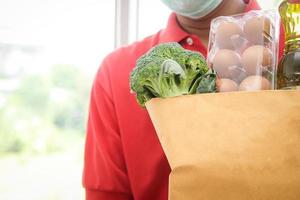 asiatisk leverans man bär en mask innehar mat, ägg, grönsaker, Ingredienser levereras till de kund. företag begrepp av mat leverans service köpa uppkopplad under de coronavirus foto