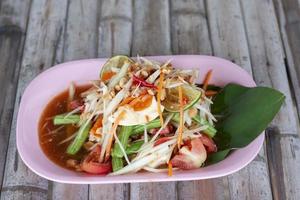 papaya sallad och saltade ägg i rosa tallrik på trä- tabell thai människor ring upp as tam thai kai khem. foto