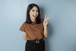 upphetsad asiatisk kvinna bär en brun t-shirt ger siffra 12345 förbi hand gest foto