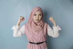 upphetsad asiatisk muslim kvinna bär en rosa hijab som visar stark gest förbi lyft henne vapen och muskler leende stolt foto