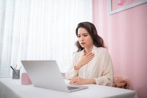 asiatisk skön kvinna sjuk med känsla smärta i de bröst medan arbetssätt med en bärbar dator foto