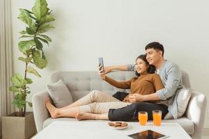 glad par tar en selfie med en smartphone på Hem Sammanträde på soffa foto