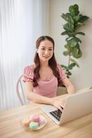 leende asiatisk kvinna använder sig av bärbar dator på Hem. frilansare. foto