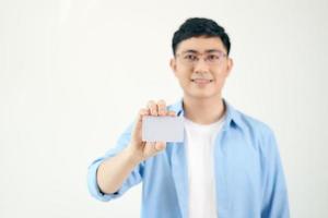 porträtt av leende asiatisk man innehav vit tom företag kort på vit bakgrund foto