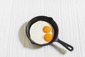 hälsosam frukost mat stekt ägg i stekpanna på vitt träbord. foto