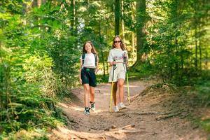 Tonårs flickor gående genom de skog. vältrampad skog spår för gående. de flickor bära en ryggsäck och gående pinnar foto