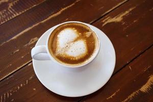 hjärtform latte art i vit kaffekopp på träbord i caférestaurang foto