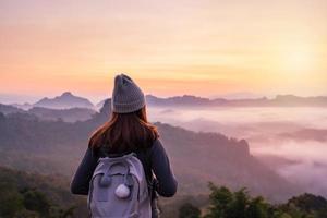 ung kvinna resande ser på hav av dimma och solnedgång över de berg foto