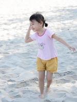 positiv charmig 4 år gammal söt bebis asiatisk flicka, liten preschooler barn stående på sand strand på skön solig dag i sommar tid. foto