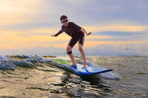 ung pojke unge surfare ridning vågor med mjuk styrelse i rayong strand, thailand. nybörjare surfingbräda studerande spelar på vatten i upphetsad ansikte och rolig handling. foto