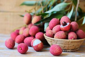 litchi skiva skalad på trä- - färsk litchi med grön löv skörda i korg från träd tropisk frukt sommar i thailand foto