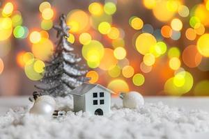 abstrakt första advent jul bakgrund. leksak modell hus och vinter- dekorationer ornament på bakgrund med snö och defocused krans lampor. jul med familj på Hem begrepp. foto