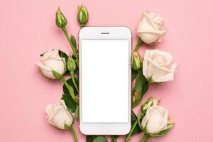 mobil telefon med ro blommor på rosa pastell bakgrund, kvinnor teknologi begrepp foto