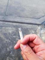 stänga upp hand av man innehav cigarett med väg eller gata bakgrund. rökning, dålig hälsa och cancer begrepp foto