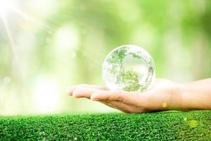 mänsklig hand innehav klot planet glas i grön skog med bokeh natur lampor. värld miljö dag. begrepp för miljö bevarande, skydda ekologi jord och miljö- miljövänlig liv. foto