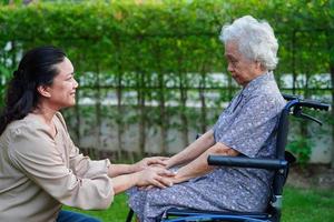 vårdgivare hjälpa asiatisk äldre kvinna funktionshinder patient sitter på rullstol i parken, medicinsk koncept. foto