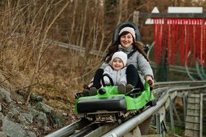 mor med dotter rida elektrisk släde på skenor. foto